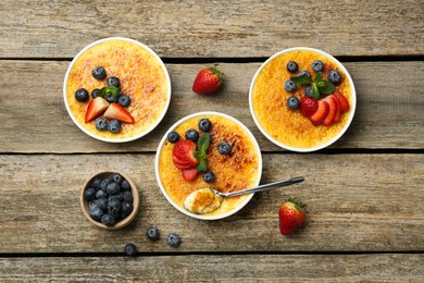 Flat lay composition with delicious creme brulee with berries and mint in bowls on wooden table