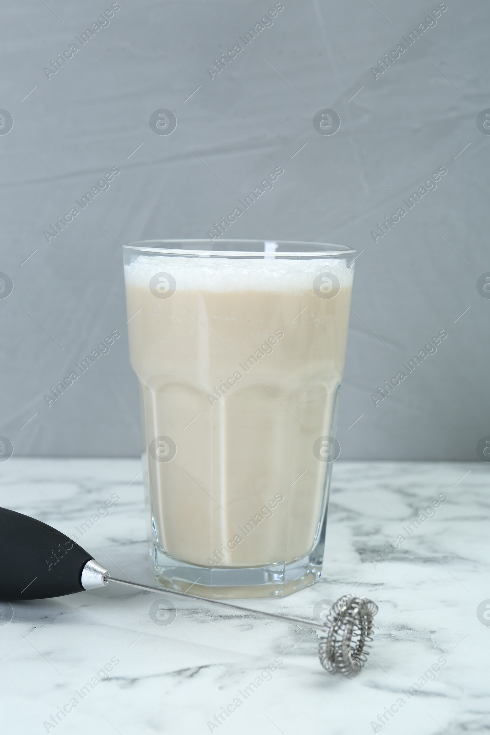 Photo of Mini mixer (milk frother) and tasty cappuccino in glass on white marble table