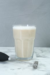 Photo of Mini mixer (milk frother) and tasty cappuccino in glass on white marble table