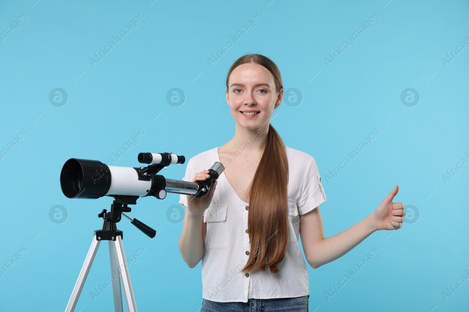 Photo of Happy astronomer with telescope showing thumbs up on light blue background