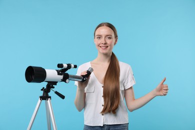 Happy astronomer with telescope showing thumbs up on light blue background