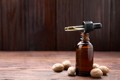Photo of Bottle of nutmeg oil, pipette and nuts on wooden table. Space for text