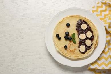 Photo of Stack of delicious crepes with fresh berries, chocolate and banana on white wooden table, top view. Space for text