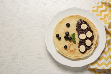 Stack of delicious crepes with fresh berries, chocolate and banana on white wooden table, top view. Space for text