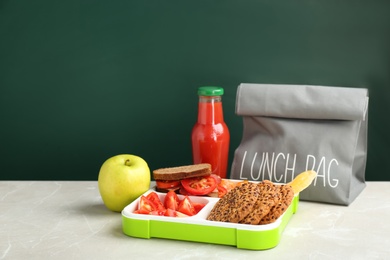 Lunch box with appetizing food and bag on table near chalkboard