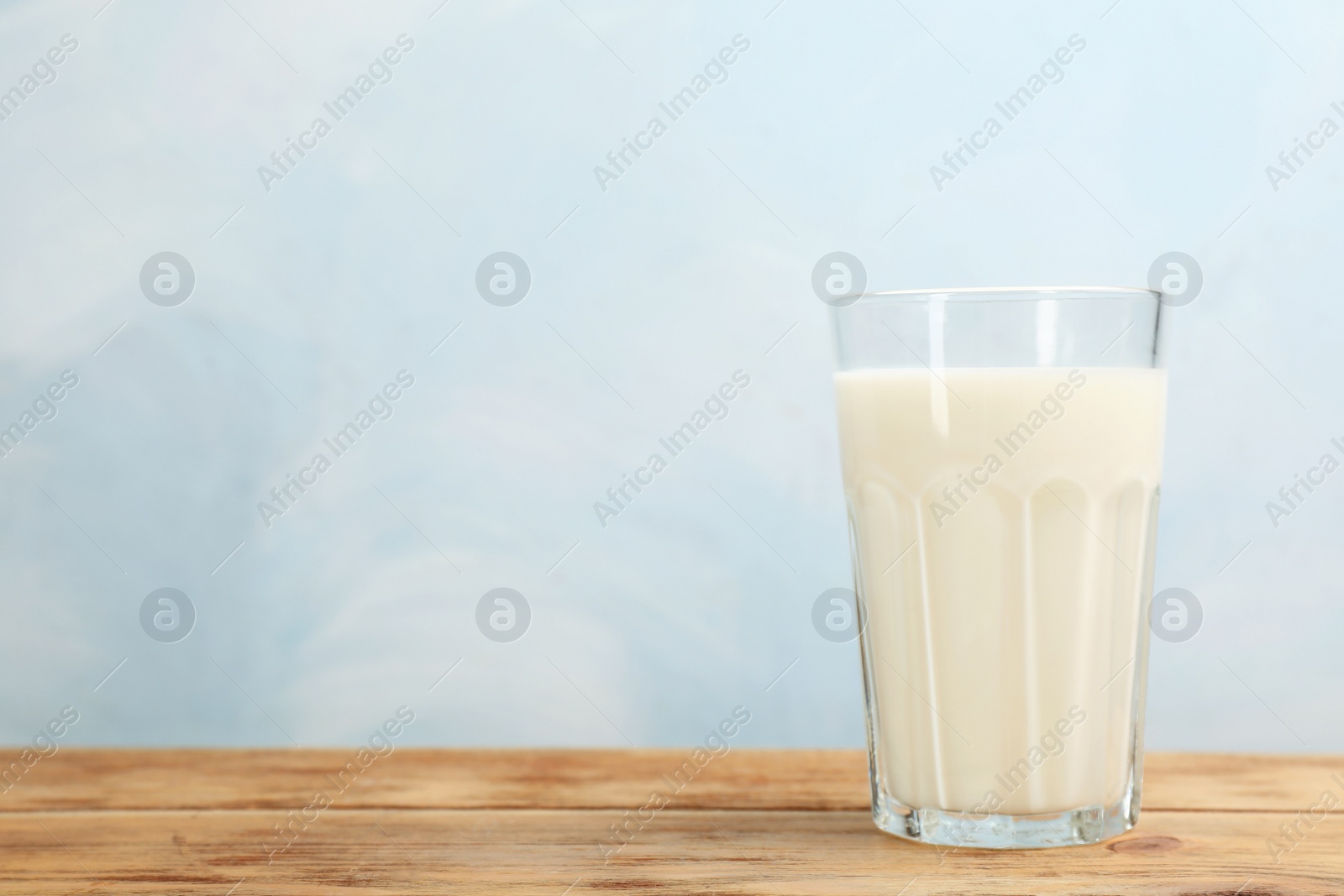 Photo of Glass with fresh milk on table against color background. Space for text