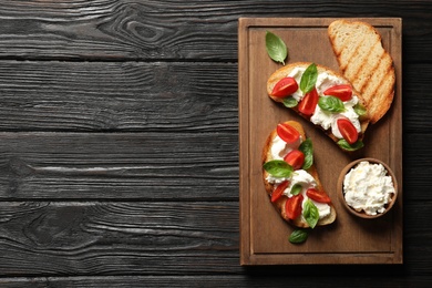 Photo of Toasted bread with tasty cream cheese and tomatoes on wooden table, flat lay. Space for text