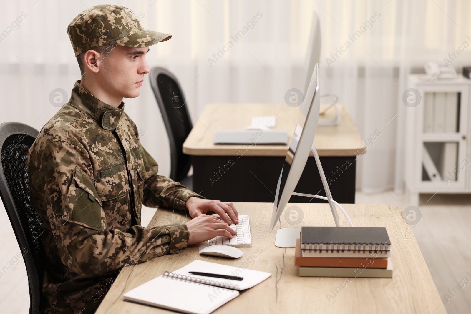 Photo of Military service. Young soldier working with computer at wooden table in office