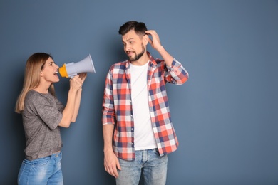 Young woman with megaphone shouting at man on color background