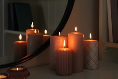 Beautiful burning candles on white console table near mirror indoors