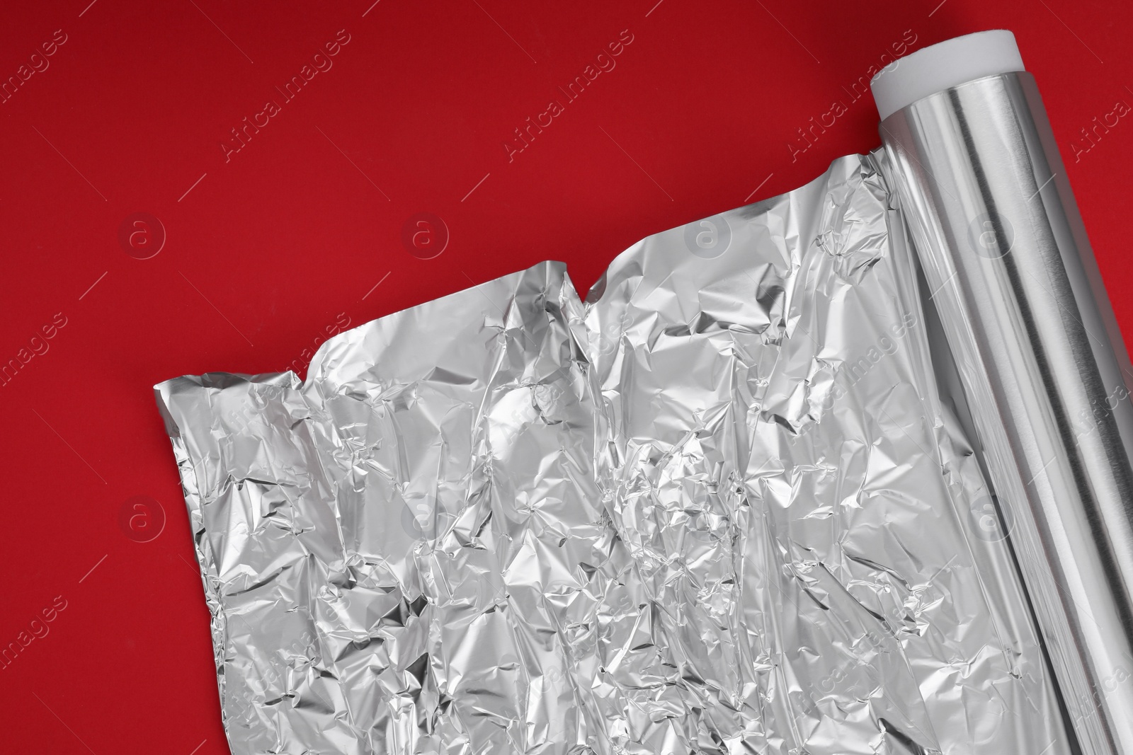 Photo of Roll of aluminum foil on red background, top view. Space for text
