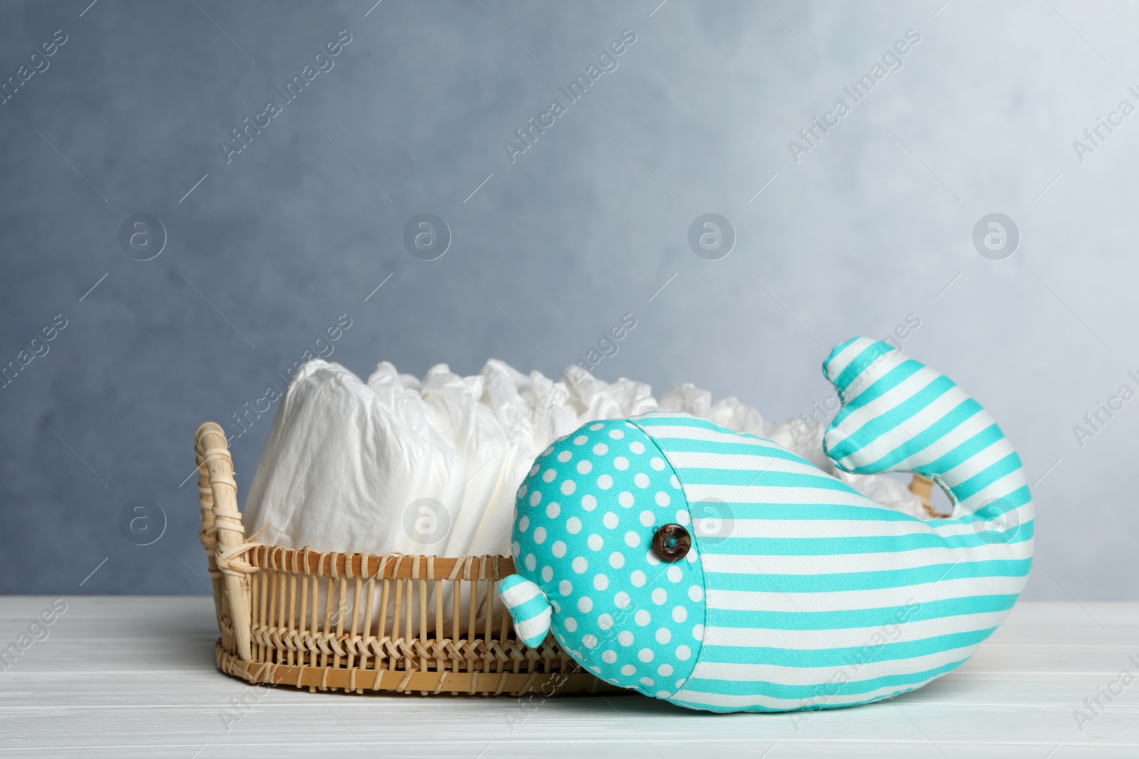 Photo of Tray with baby diapers and toy on white wooden table against grey background