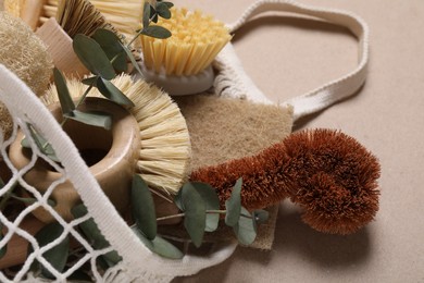 Photo of Cleaning brushes, sponges, eucalyptus leaves and string bag on pale brown background, closeup