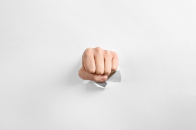 Photo of Woman showing clenched fist through hole in torn white paper, closeup. Victory concept