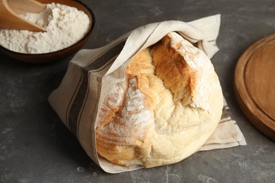 Photo of Loaf of fresh bread wrapped in fabric on grey table