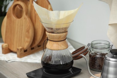 Photo of Glass chemex coffeemaker with paper filter and coffee on wooden countertop in kitchen