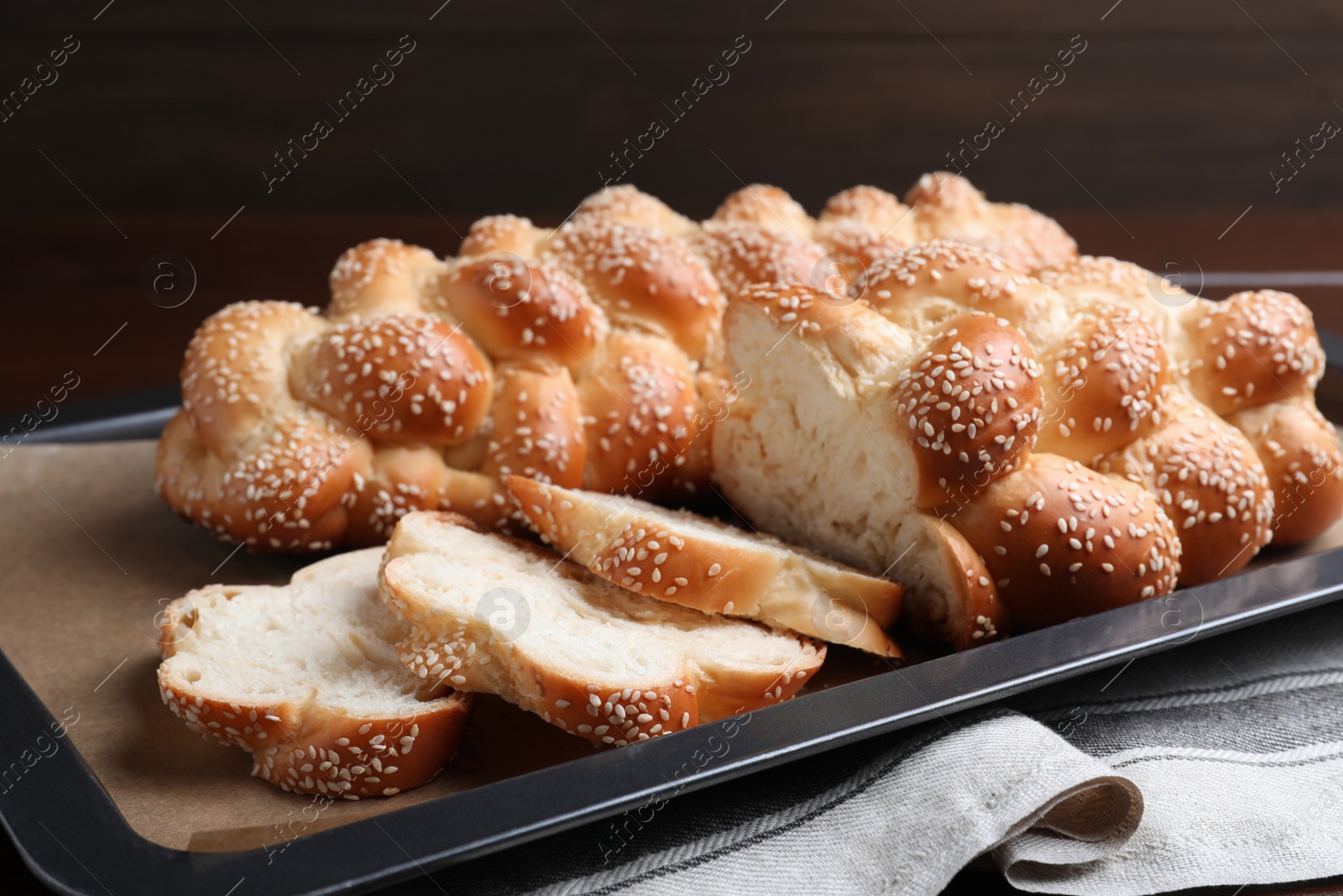 Photo of Baking tray with homemade braided bread on wooden table, closeup. Challah for Shabbat