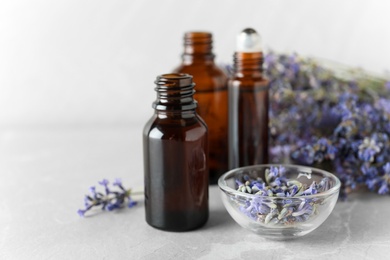 Bottles of essential oil and lavender flowers on stone table against light background. Space for text