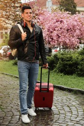 Tourist with headphones and stylish suitcase on city street