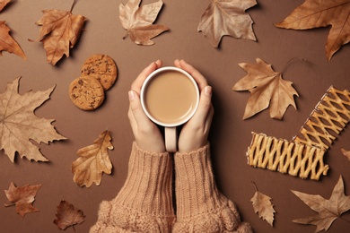 Photo of Woman in autumn sweater holding hot cozy drink on color background, top view