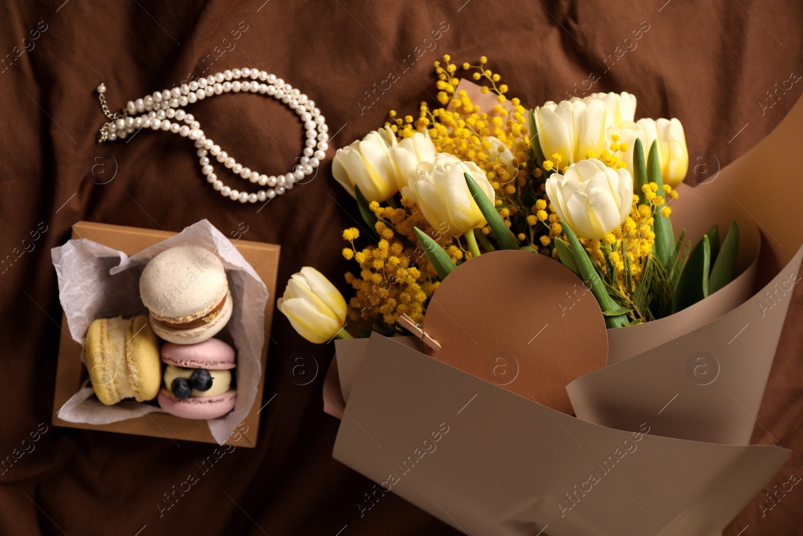 Photo of Bouquet of beautiful spring flowers, macarons and necklace on brown fabric, flat lay