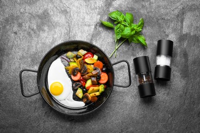 Photo of Pan with tasty cooked egg and vegetables on grey table, flat lay
