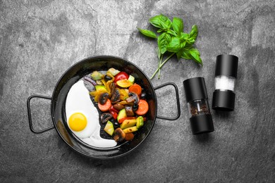 Pan with tasty cooked egg and vegetables on grey table, flat lay