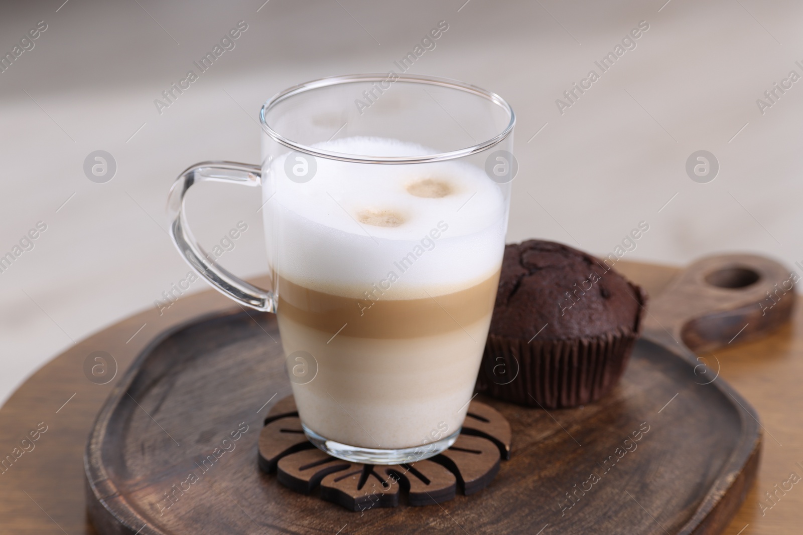 Photo of Cup of aromatic latte macchiato and chocolate muffin on table against light background, closeup