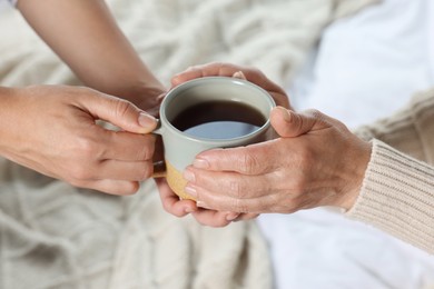 Photo of Caregiver giving drink to elderly woman at home, closeup