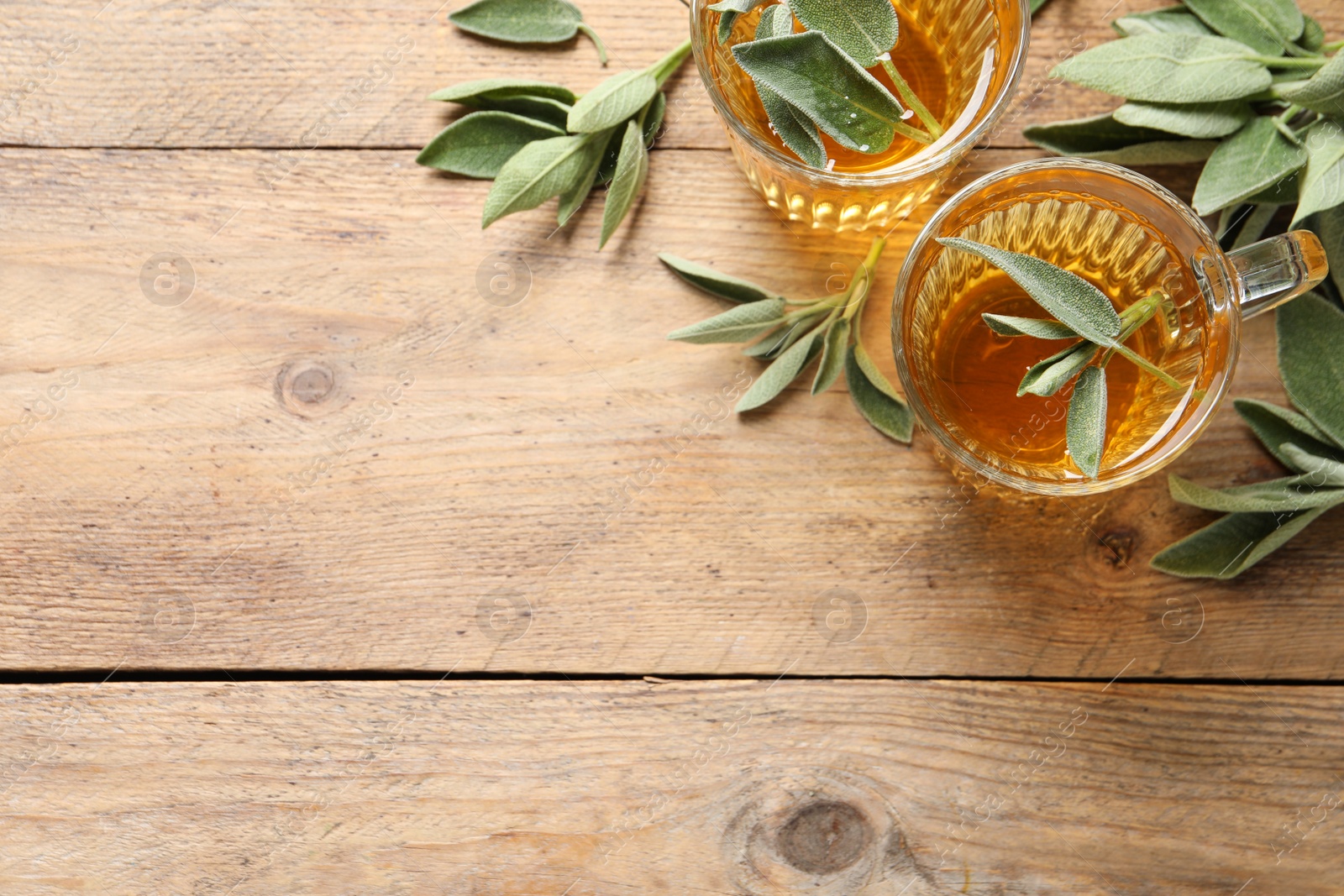 Photo of Cups of aromatic sage tea and fresh leaves on wooden table, flat lay. Space for text