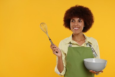 Photo of Happy young woman in apron holding bowl and whisk on orange background. Space for text