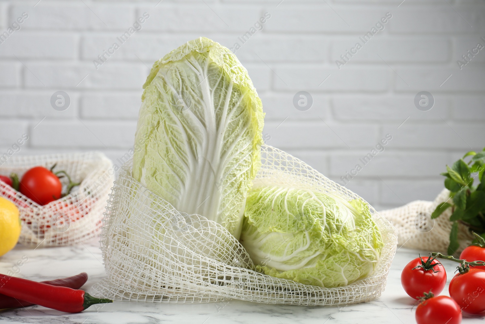 Photo of Fresh Chinese cabbages and other vegetables on white marble table near brick wall