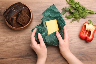 Photo of Woman packing piece of cheese into beeswax food wrap at wooden table, top view