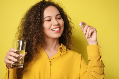 Photo of African-American woman with glass of water and vitamin pill on yellow background