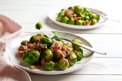 Photo of Delicious Brussels sprouts with bacon on white wooden table