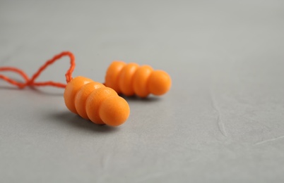 Photo of Pair of orange ear plugs with cord on grey background, closeup. Space for text