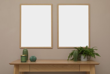 Photo of Empty frames hanging on beige wall over wooden table with decor. Mockup for design