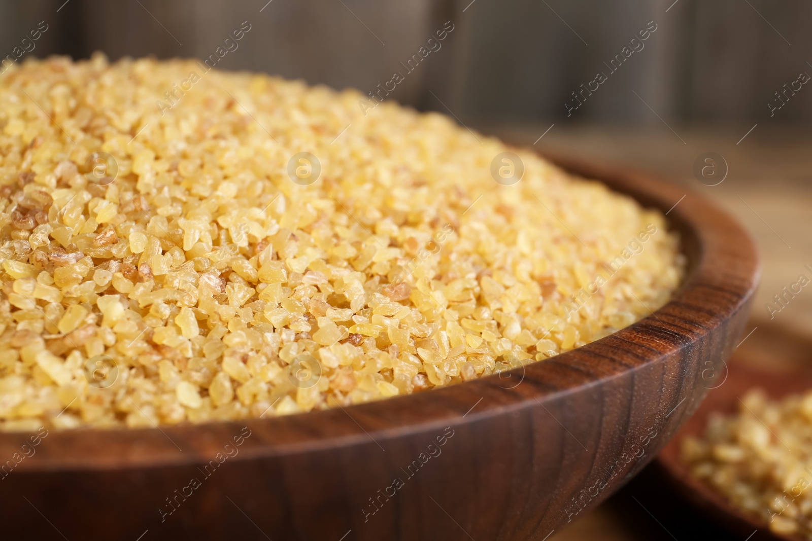 Photo of Bowl with uncooked bulgur on wooden table, closeup