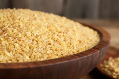 Bowl with uncooked bulgur on wooden table, closeup