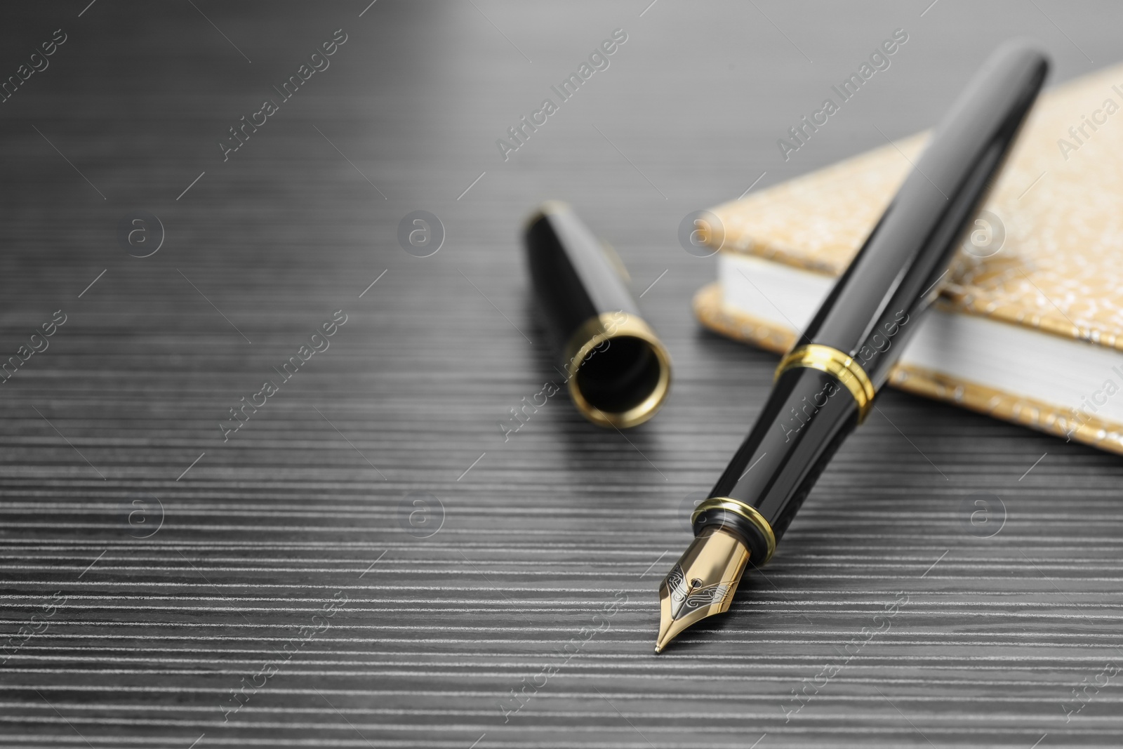 Photo of Stylish fountain pen and notebook on black wooden table, closeup. Space for text