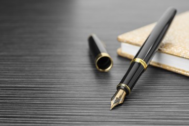 Photo of Stylish fountain pen and notebook on black wooden table, closeup. Space for text