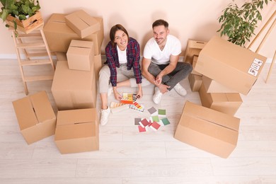 Happy couple surrounded by moving boxes choosing colors in new apartment, above view