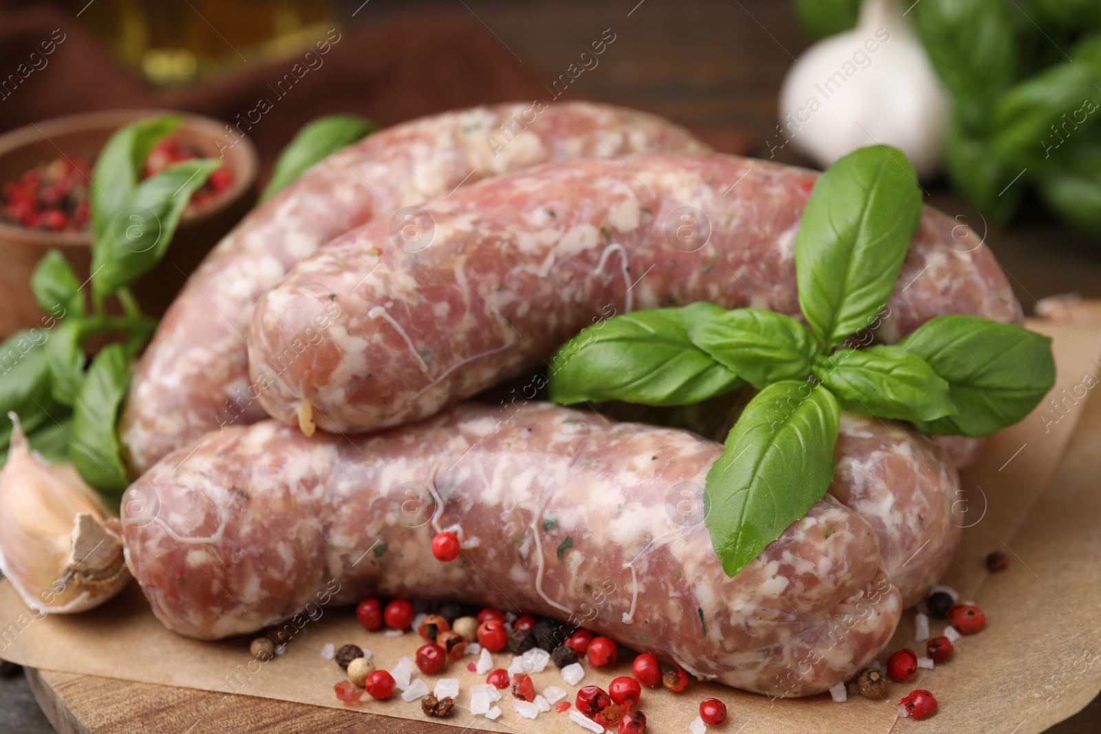 Photo of Raw homemade sausages and different spices on wooden board, closeup