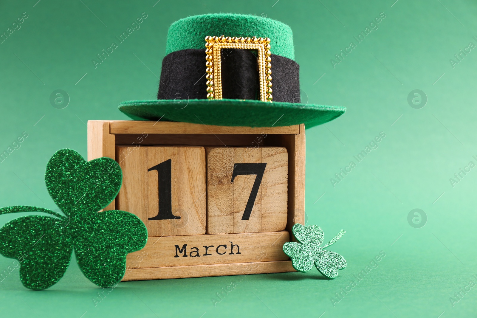 Photo of St. Patrick's day - 17th of March. Wooden block calendar, leprechaun hat and decorative clover leaves on green background