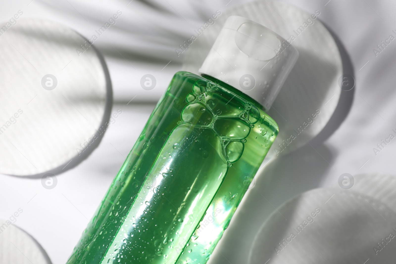 Photo of Wet bottle of micellar water and cotton pads on white background, closeup