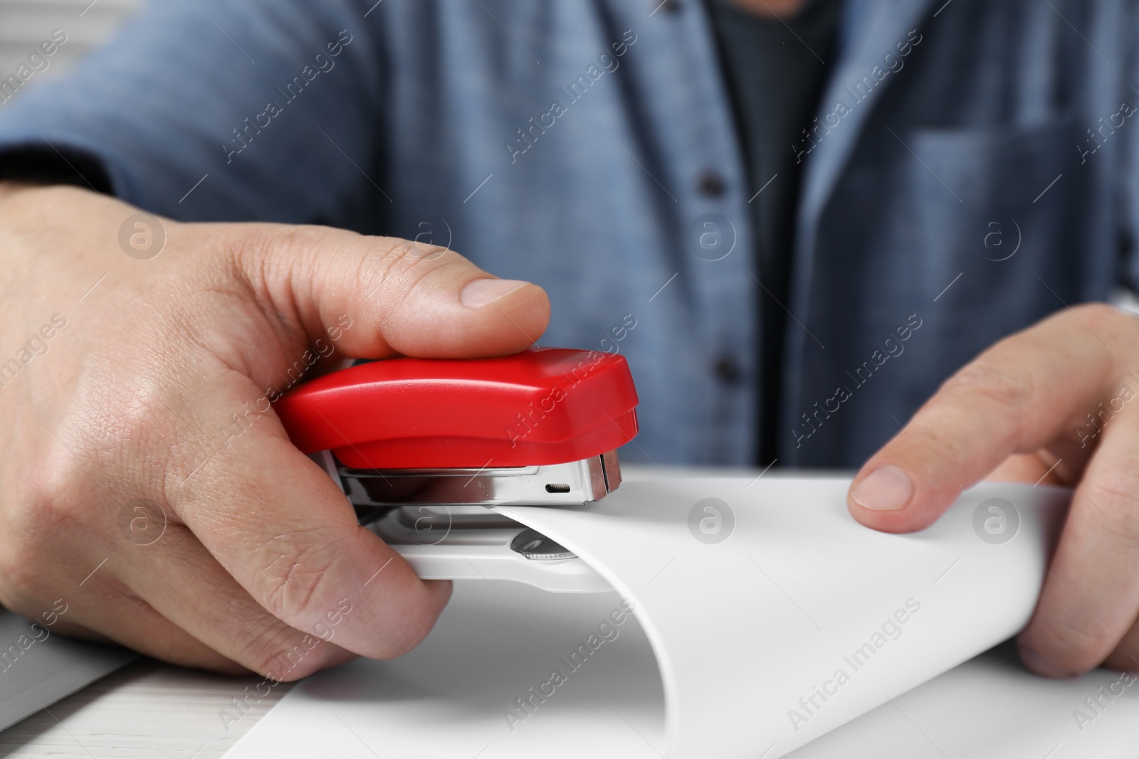 Photo of Man with papers using stapler at white table, closeup