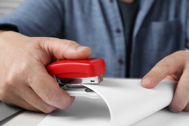 Man with papers using stapler at white table, closeup