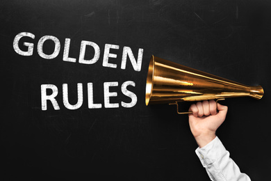 Image of Man holding retro megaphone near chalkboard with phrase GOLDEN RULES, closeup