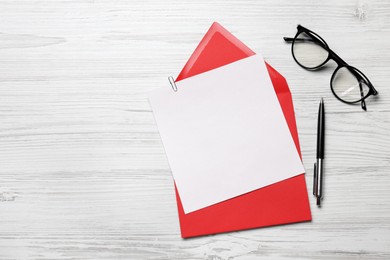 Photo of Envelope with blank paper card, glasses and pen on white wooden table, flat lay. Space for text