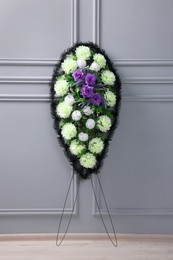 Funeral wreath of plastic flowers near light grey wall indoors